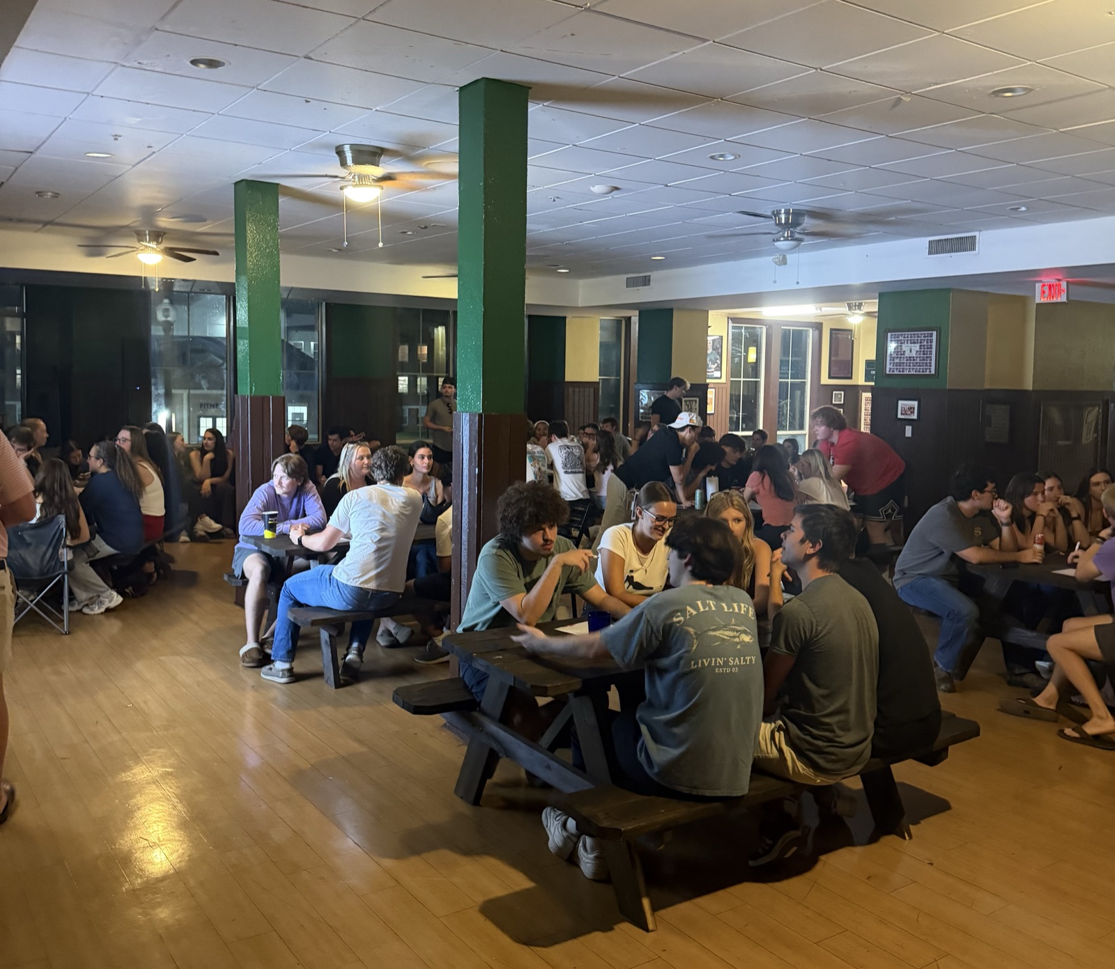 Brothers and Alpha Omicron Pi sisters seated at picnic tables in the chapter room during trivia night