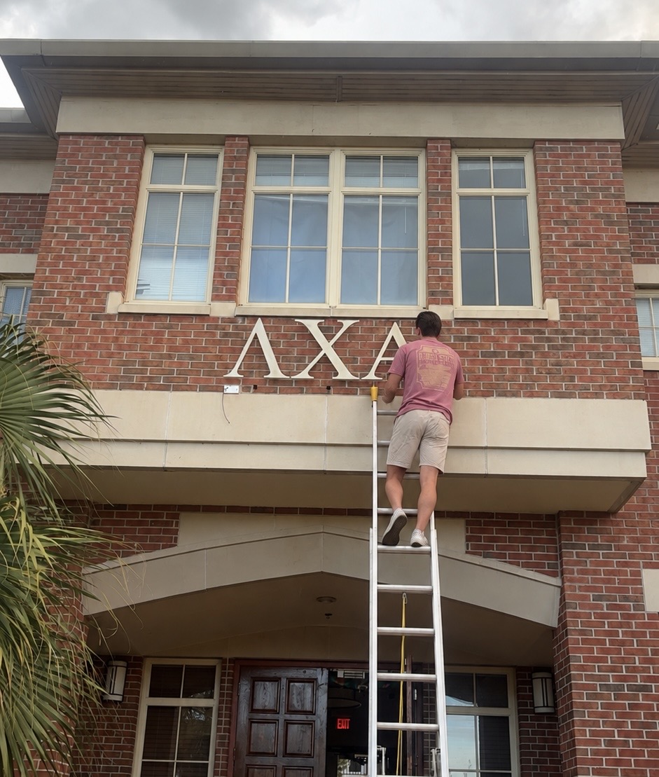 Brother Alex den Boggende on a ladder mounting the Lambda Chi Alpha letters above the front entrance of the chapter house